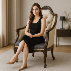 Woman in a black dress sitting on an ornate chair in a room with a lamp and vase.
