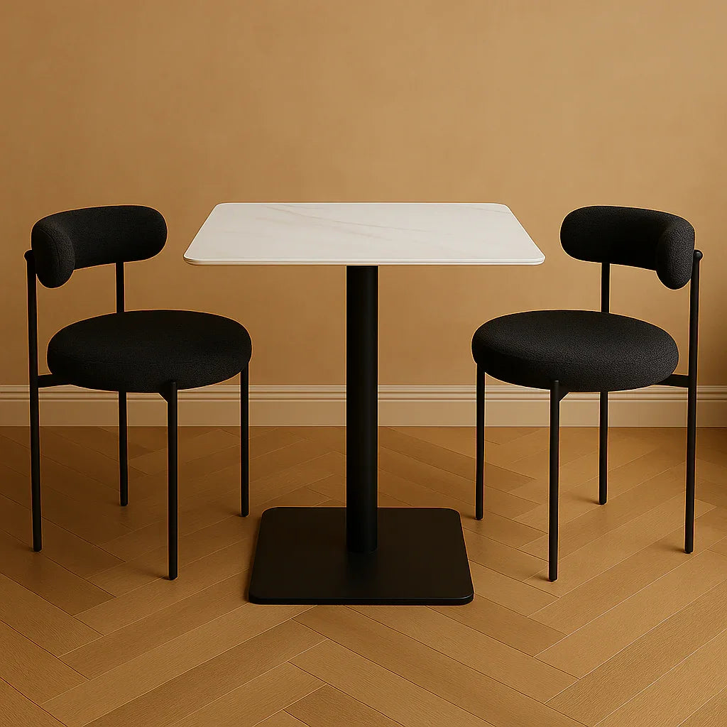 Two black chairs with cushioned seats and backrests are arranged around a white square table on a wooden floor.