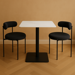 Two black chairs with cushioned seats and backrests are arranged around a white square table on a wooden floor.