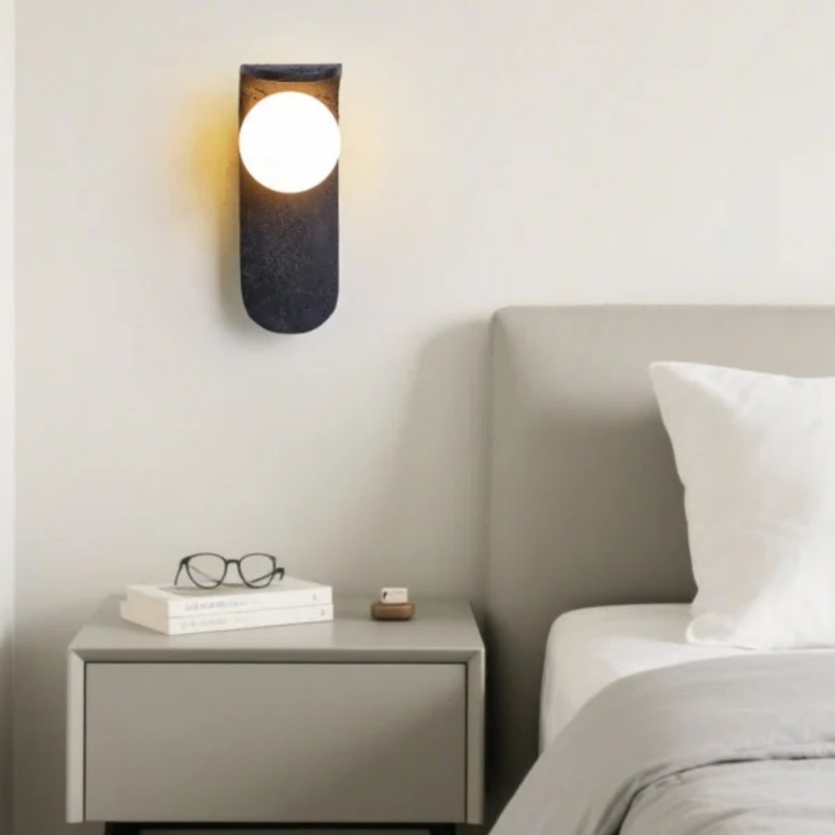 Skatera Travertine Wall Lamp above a nightstand with books and glasses