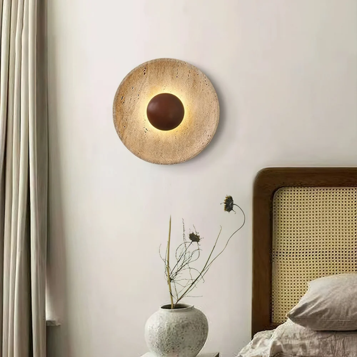 Solara Travertine Round Wall Light above a rattan headboard bed with linen bedding and ceramic vase