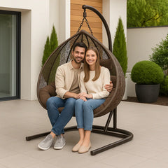 Man and woman sitting in a hanging egg chair outdoors with plants in the background