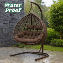 Brown wicker hanging chair with cushions on a patio, surrounded by greenery.