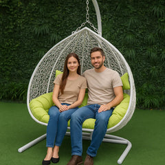 Two people sitting in a hanging egg chair with a green background