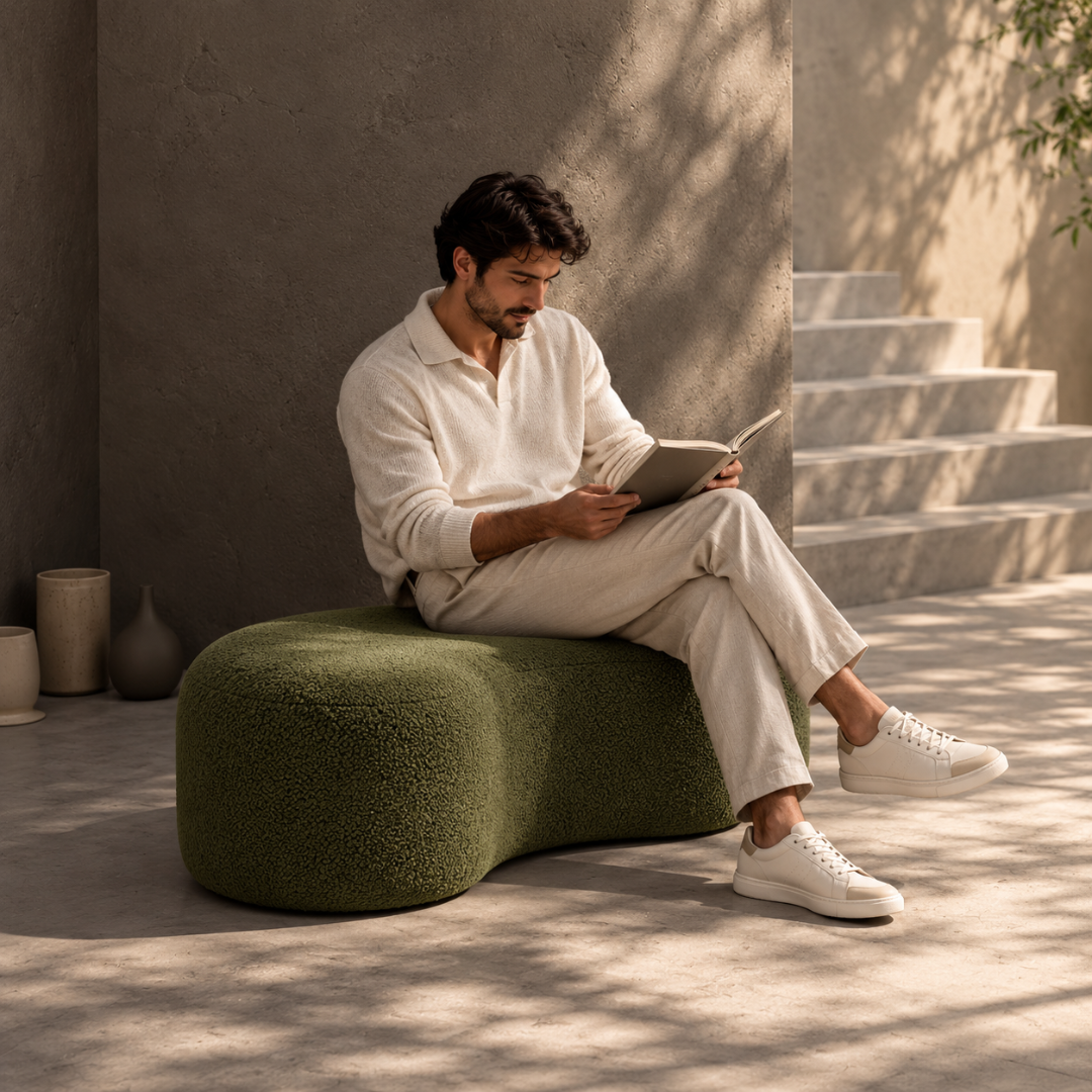 Man reading while sitting on the Fern curved olive boucle bench ottoman