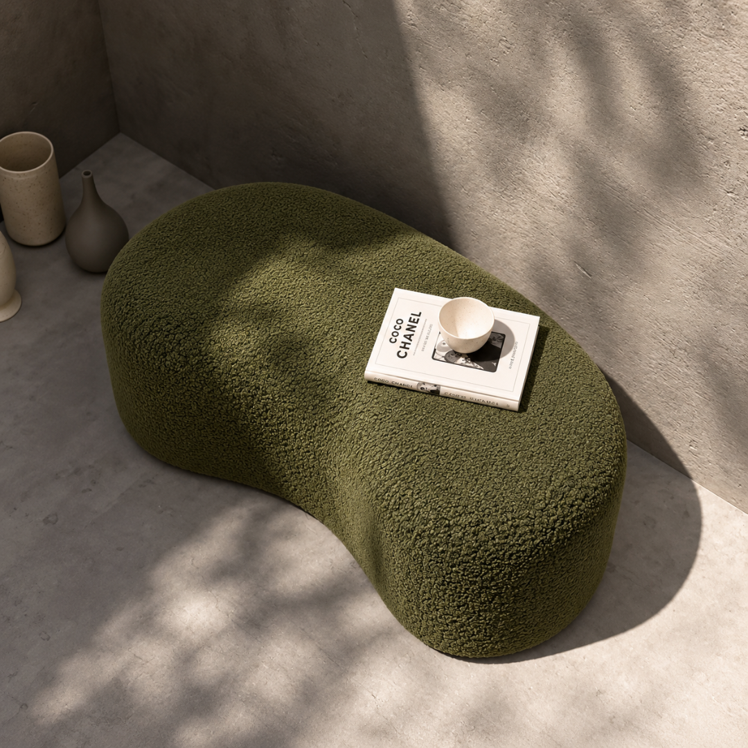 Top view of the Fern organic bean-shaped boucle ottoman with a book and cup
