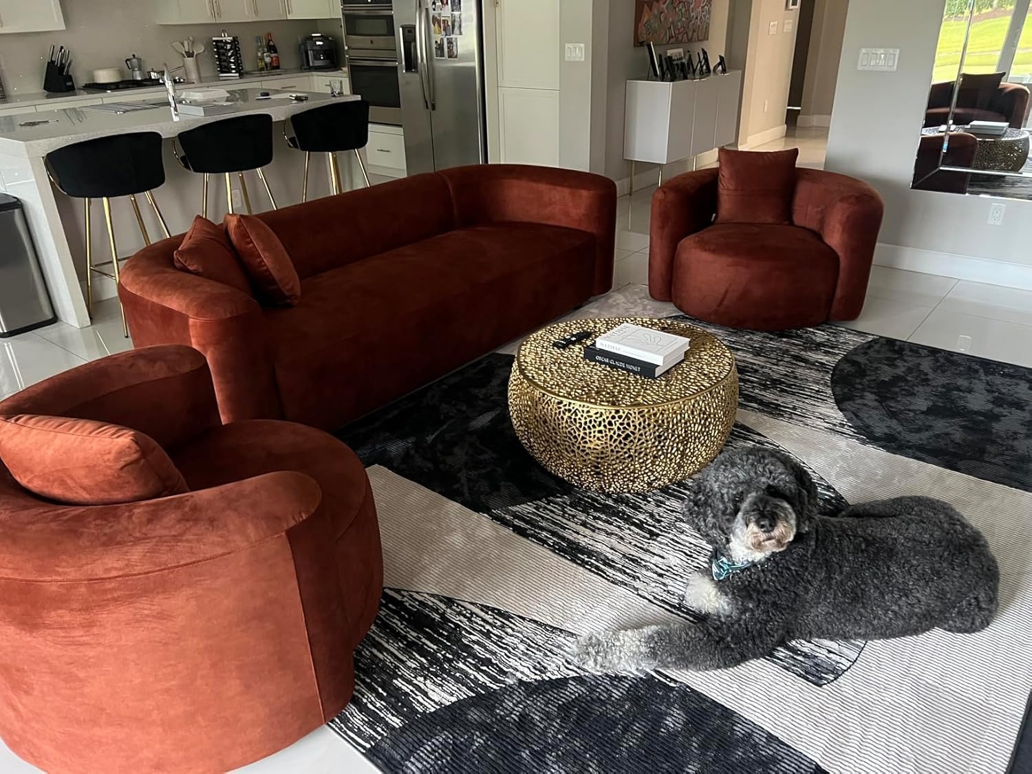 Modern living room with red velvet sofa, armchair, and ottoman on a patterned rug.