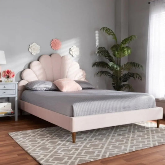 Modern bedroom interior featuring a pastel pink upholstered bed with a scalloped headboard, grey bedding, decorative pillows, wooden flooring, and indoor plants.