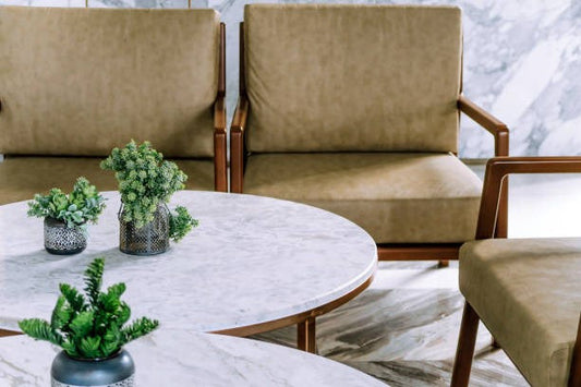 Modern seating area with upholstered armchairs and a sofa in neutral tones, paired with round marble-top coffee tables and small potted plants in a contemporary indoor setting.
