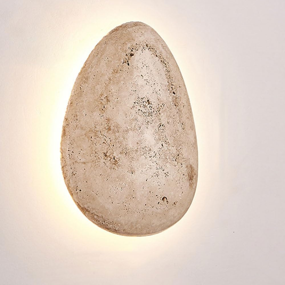 front view of the organic pebble-shaped travertine wall sconce, lit on a plain background