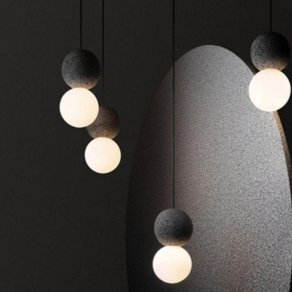 close-up of three Mia Orb pendants at different heights beside a curved stone wall element, dark background