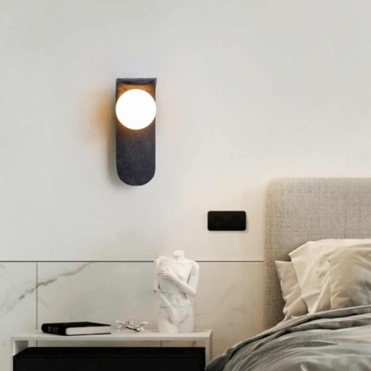 Skatera Travertine Wall Lamp above a nightstand with a sculptural bust decor piece