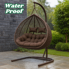 Brown wicker hanging chair with cushions on a patio, surrounded by greenery.